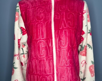 May include: A pink fleece jacket with a white zipper and the word "Juicy" embossed on the front. The sleeves are white with a strawberry pattern and the word "Juicy" in cursive. The jacket has a high collar and a soft texture.