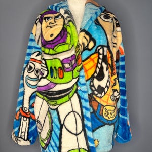 May include: A soft, hooded robe featuring characters from the animated film Toy Story. The robe displays Buzz Lightyear, Woody, and Forky in bright colours. The robe has a blue striped pattern on the sleeves and hood.