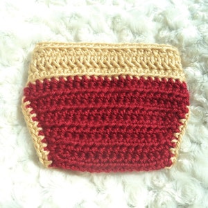 Puede incluir: Cubierta de pa&ntilde;al de crochet rojo con un borde de crochet dorado.