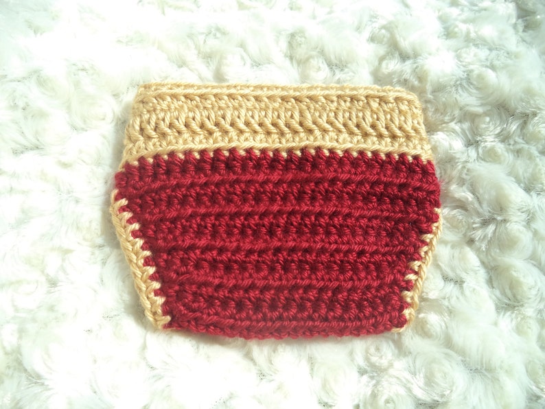 Puede incluir: Cubierta de pa&ntilde;al de crochet rojo con un borde de crochet dorado.