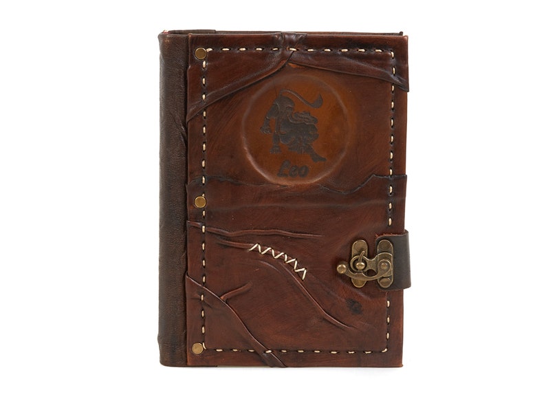 May include: Brown leather journal with a stitched border and a brass clasp. The front cover features an embossed lion with the word "Leo" underneath.
