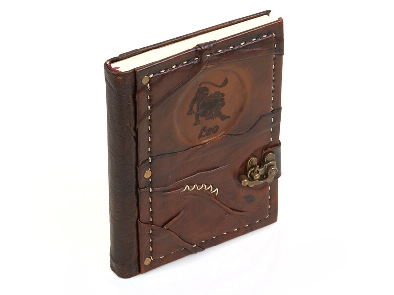 May include: Brown leather journal with a stitched design and a brass clasp. The front cover features an embossed lion with the word "Leo" underneath.