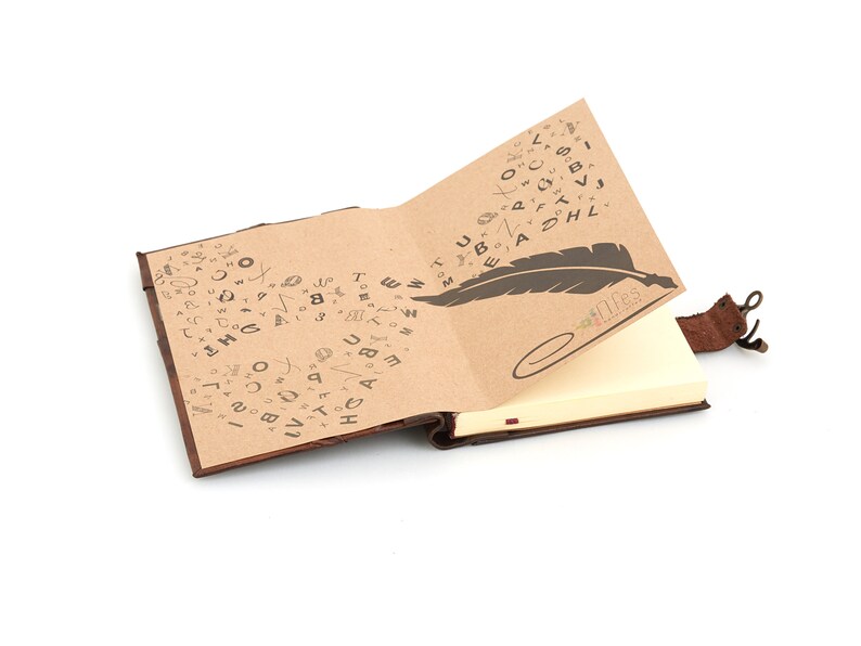 May include: A brown leather-bound journal with a blank page open. The cover is decorated with a pattern of handwritten letters and a feather quill. The journal has a leather strap with a metal clasp.