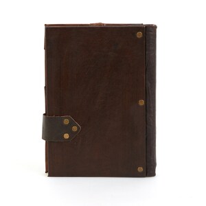 May include: A brown leather-bound journal with a strap closure and brass accents. The journal has a rustic and vintage aesthetic.