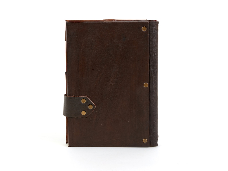 May include: A brown leather-bound journal with a strap closure and brass accents. The journal has a rustic and vintage aesthetic.
