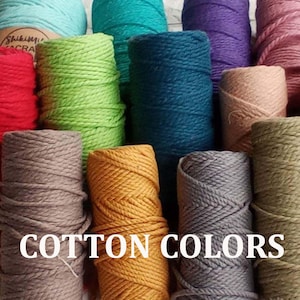 Op de afbeelding: Een assortiment katoenen touw in verschillende kleuren, waaronder turquoise, groen, grijs, bruin en oranje. Het touw is in een halve cirkel gerangschikt met de tekst "COTTON COLORS" in witte letters onderaan.