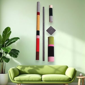 May include: A set of five wall-mounted decorative pieces. The pieces are made of different materials and colors, including wood, yarn, and fabric. The pieces are arranged in a vertical line, with the tallest piece on the left and the shortest piece on the right. The pieces are all different lengths and widths, and they are all different colors. The pieces are all different textures, and they are all different shapes.
