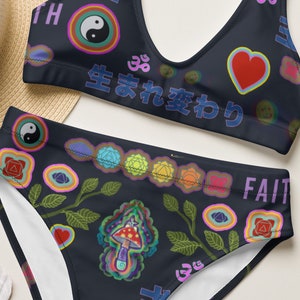 Könnte beinhalten: Ein zweiteiliges Bikini-Set mit dunkelblauem Hintergrund und farbenfrohen, skurrilen Designs. Das Oberteil und die hoch taillierten Unterteile zeigen Herzen, Yin-Yang-Symbole und japanischen Text. Das Wort "FAITH" ist auf der Unterseite aufgedruckt.