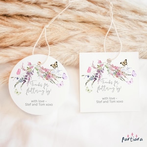 Puede incluir: Dos etiquetas de agradecimiento redondas y cuadradas con un diseño floral y mariposas. El texto en las etiquetas dice "Gracias por revolotear!" con amor - Stef y Tom xoxo.