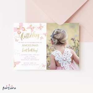 Pode incluir: Convite para a festa de primeiro aniversário com tema de borboletas rosa e douradas com uma foto de uma menina pequena usando um vestido rosa com um design de borboleta nas costas. O convite inclui o texto "flutterby" em escrita dourada, "Para celebrar o primeiro aniversário de Angelina!" e os detalhes da festa.