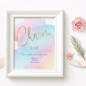 May include: A white frame with a pastel watercolor background and gold lettering that reads "Charm Bar". The text below reads "Choose one of these items and get creating!" with a list of items: Necklace, Bracelet, Key Chain.