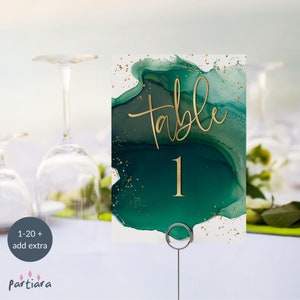 Puede incluir: Tarjeta de número de mesa verde y dorada con la palabra "Mesa" y el número "1" en letras doradas. La tarjeta tiene un diseño abstracto verde y dorado.