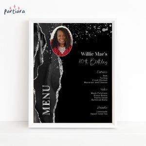 May include: A rectangular menu sign featuring a black background with a silver glittery abstract edge. It includes a circular photo of a person, the text Willie Mae's 80th Birthday, and a list of food items under the headings Entrées, Sides, and Drinks.