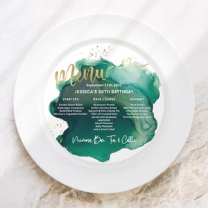 Op de afbeelding: Een wit bord met een groen en gouden aquarelontwerp. Het bord heeft een menu voor Jessica's 50e verjaardag met een lijst van voorgerechten, hoofdgerechten en desserts. De tekst "Mimosa Bar Tea & Coffee" staat onderaan het bord.