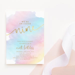 Puede incluir: Una invitación pastel de acuarela con letras doradas que dice "We're on Cloud Nine" y "Isabella's ninth birthday". La invitación incluye detalles del evento. Una cinta blanca y un sobre rosa están en el fondo.