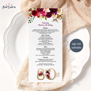 May include: A menu card for an 80th birthday celebration. The card features a floral design with burgundy and pink flowers. The menu includes starters, main courses, sides, and desserts. The text "age not editable" is also visible.