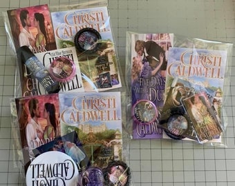 May include: Two clear plastic bags filled with various romance novels and buttons. The novels are by author Christi Caldwell and feature images of couples on the covers. The buttons are round and feature images of couples and the author's name.