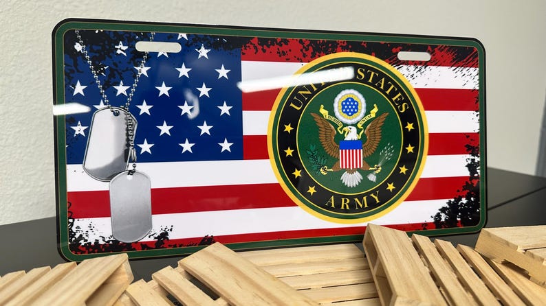 May include: A metal licence plate with a distressed American flag design. The centre features the United States Army seal with an eagle and the words "United States Army". Two silver dog tags hang from a chain.