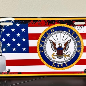 May include: A metal licence plate featuring a distressed American flag with a navy blue seal that reads "United States Navy". Two silver dog tags hang from the top of the plate.