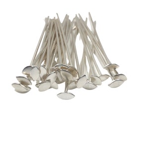 May include: A pile of silver-toned head pins with flat, oval-shaped heads. The pins are arranged in a random pattern.