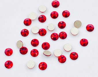May include: A scattering of red rhinestones on a white background. The rhinestones are round and have a flat back.