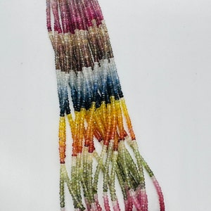 May include: A strand of colourful gemstone beads, featuring shades of pink, red, orange, yellow, green, blue, and purple. The beads are faceted and have a slightly irregular shape.