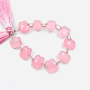 May include: A strand of pink rose quartz beads, each bead is shaped like a flower with faceted edges. The beads are strung on silver wire and have a pink tassel at one end.