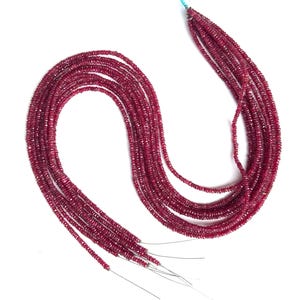 Könnte beinhalten: Mehrere Stränge kleiner, tiefroter Rubinperlen. Die Perlen sind aufgefädelt und bilden leicht gebogene Stränge. Die Perlen haben eine gleichmäßige Größe und Form und erzeugen eine satte Farbe und Textur.