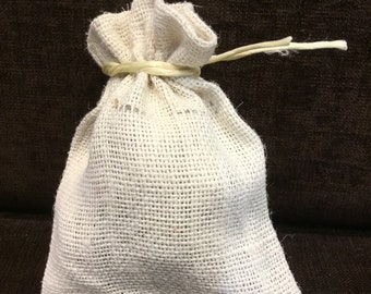 May include: A small, off-white drawstring pouch crafted from a coarse, woven fabric. The bag features a gathered top secured by a light-colored, thin cord tied in a simple knot, creating a ruffled edge at the opening of the textile container.
