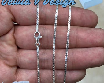 May include: Three silver box chains of varying lengths, laid out on a hand. The chains are made of small, square links. The image includes the text "Olivia V Design".