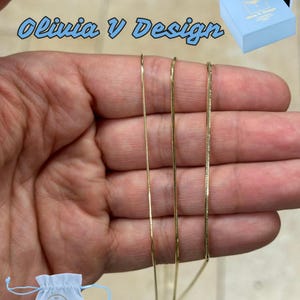 May include: Three gold chains of different widths, hanging from a hand. The chains are all the same length. The image is labeled "Olivia V Design".