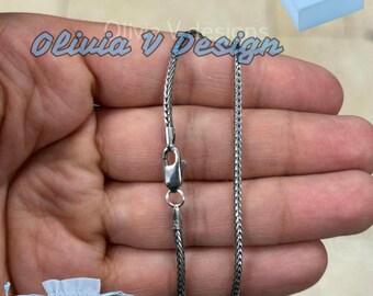 May include: A silver chain necklace with a lobster clasp. The chain is a delicate, box style chain. The necklace is displayed on a hand.