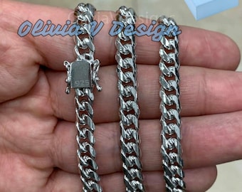 May include: A silver curb chain necklace with a lobster clasp. The chain is 925 sterling silver and is shown in a hand.