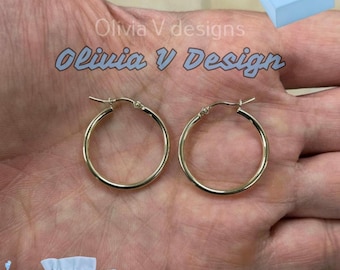 May include: A pair of gold hoop earrings on a hand. The earrings are simple and elegant, and they would make a great gift for any occasion.