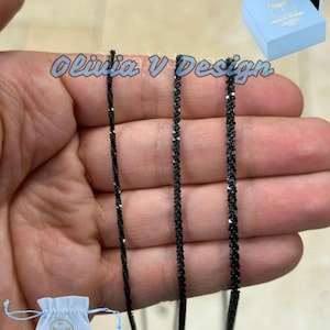May include: Three black chain necklaces with a silver sheen, displayed on a hand. The chains are of varying widths. The image includes the text "Olivia V Design".