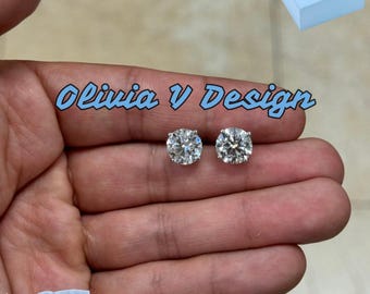 Könnte beinhalten: Ein Paar silberne Ohrstecker mit großen, klaren runden Steinen. Die Ohrringe befinden sich auf einer Hand, und der Hintergrund ist eine hellblaue Oberfläche. Der Text "Olivia V Design" ist im Bild sichtbar.