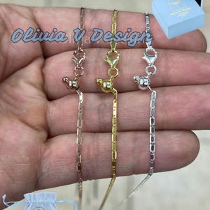 Puede incluir: Tres cadenas de oro delicadas con un peque&ntilde;o dije de bola en cada una. Las cadenas son de oro rosa, oro amarillo y plata. Las cadenas se muestran en una mano sobre un fondo azul claro.