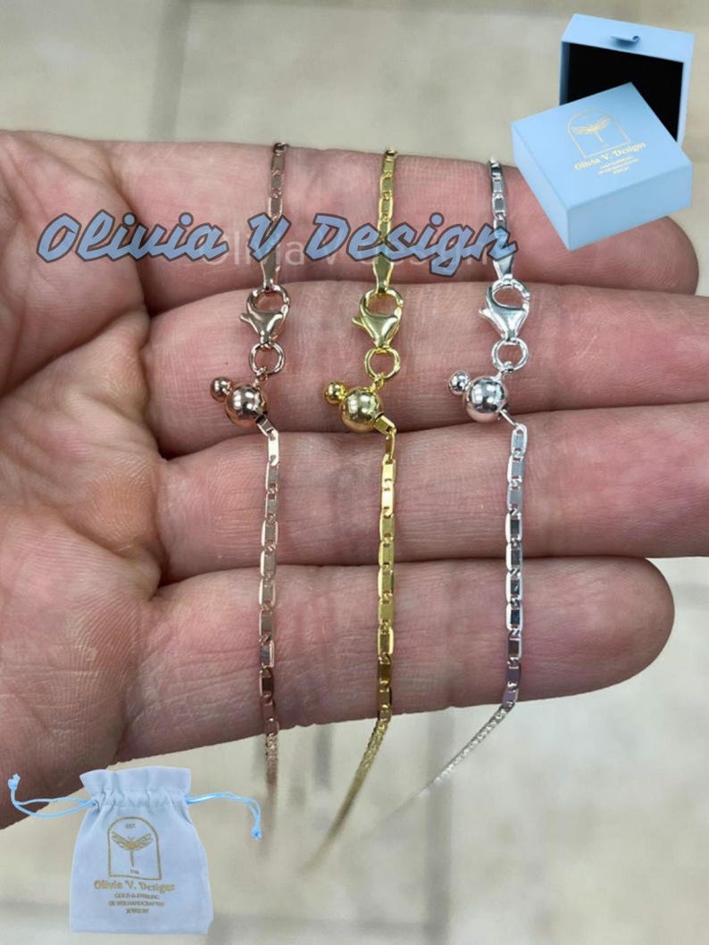 Puede incluir: Tres cadenas de oro delicadas con un peque&ntilde;o dije de bola en cada una. Las cadenas son de oro rosa, oro amarillo y plata. Las cadenas se muestran en una mano sobre un fondo azul claro.