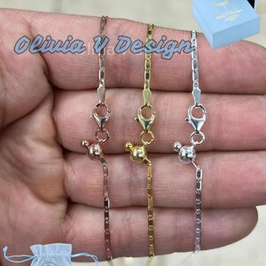 Puede incluir: Tres delicados collares de cadena con cierres magn&eacute;ticos. Las cadenas son de plata, oro y oro rosa. Los collares se muestran en una mano.