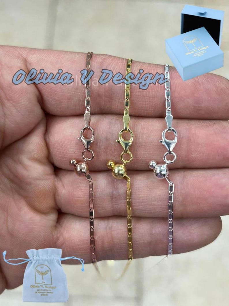 Puede incluir: Tres delicados collares de cadena con cierres magn&eacute;ticos. Las cadenas son de plata, oro y oro rosa. Los collares se muestran en una mano.