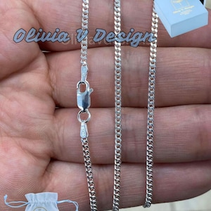 May include: A silver curb chain necklace with a lobster clasp. The chain is laid out on a hand, showing the length and width of the chain.