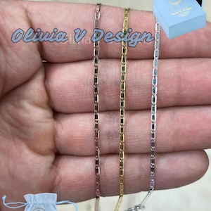 Puede incluir: Tres delicados collares de cadena en oro rosa, oro y plata. Las cadenas se sostienen en una mano y todas tienen la misma longitud. Las cadenas est&aacute;n en una caja con el texto "Olivia V Design" en ella.