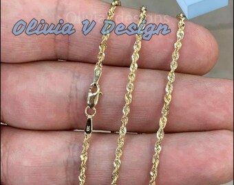 May include: A gold rope chain necklace with a lobster clasp. The chain is displayed on a hand and comes in a blue box with the text "Olivia V Design".