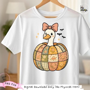 Puede incluir: Camiseta blanca con un dibujo de un ganso de dibujos animados con un lazo rosa, que emerge de una calabaza de retazos. La calabaza está hecha de patrones florales y a cuadros en naranja, amarillo y verde. También se incluyen pequeños murciélagos y estrellas.