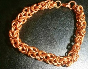 May include: A copper chain bracelet with a woven design. The bracelet is made of small, interlocking rings.