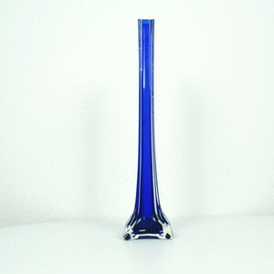 Könnte beinhalten: Eine hohe, schlanke Vase aus kobaltblauem Glas. Die Vase hat einen ausgestellten Fuß und einen langen, zylindrischen Hals. Die Vase besteht aus glänzendem Glas und steht vor einem weißen Hintergrund.