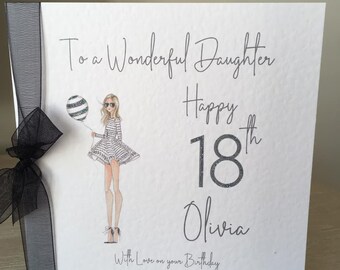 May include: White birthday card with the text "To a Wonderful Daughter Happy 18th Olivia With Love on your Birthday". The card features an illustration of a woman holding a balloon and a black ribbon.