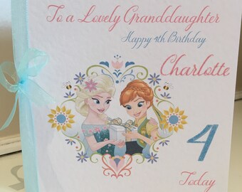 May include: A square birthday card with a light blue ribbon. The card features the text "To a Lovely Granddaughter Happy 4th Birthday Charlotte Today". It has illustrations of Elsa and Anna from Frozen.