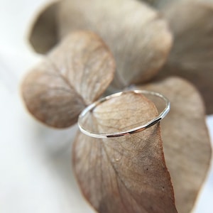 Puede incluir: Un fino anillo de plata con textura martillada, descansando sobre una hoja seca.