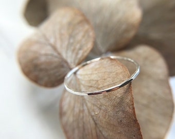 May include: A thin silver ring with a hammered texture, resting on a dried leaf.